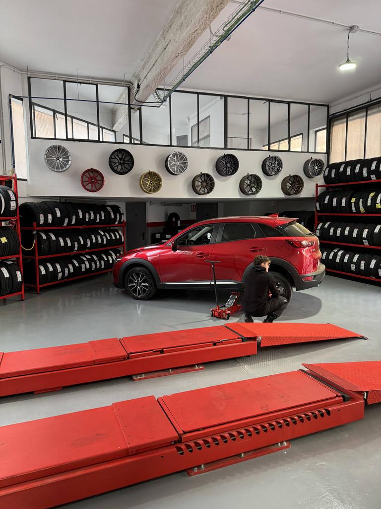 Interior taller pneumáticos Toni con neumáticos, llantas, y un operario arreglando un coche rojo